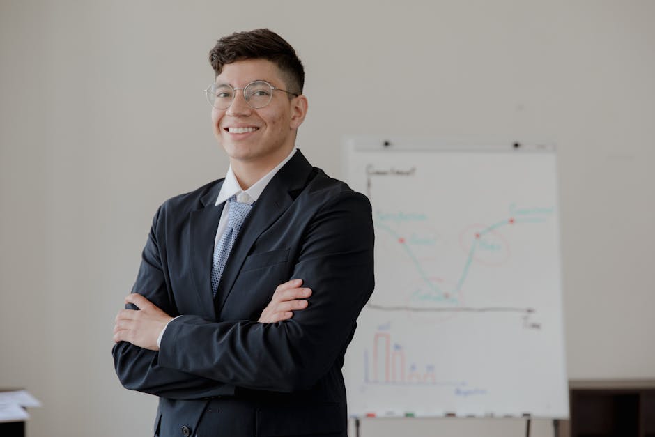 A smiling businessman with crossed arms in a formal suit stands near a whiteboard.